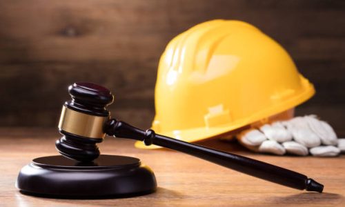 Judge Gavel In Front Of Yellow Safety Helmet On The Wooden Table